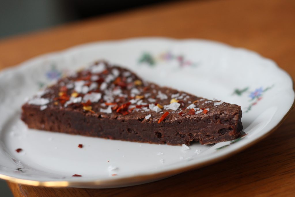 En bit kladdkaka på en tallrik, garnerad med chili flakes och havssalt.